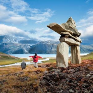 A man and child are taking in the view of the mountains beside an inukshuk in Labrador.