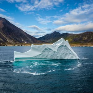 A massive iceberg is floating by an ancient mountain range.