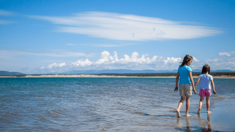 Two young girls are walking along the shore at Shallow Bay Beach.