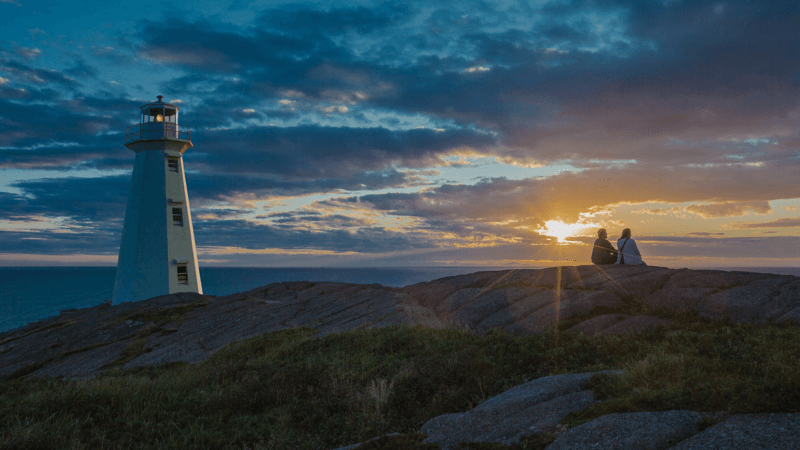 Two travellers are watching the first sunrise in North America at Cape Spear Lighthouse National Historic Site.