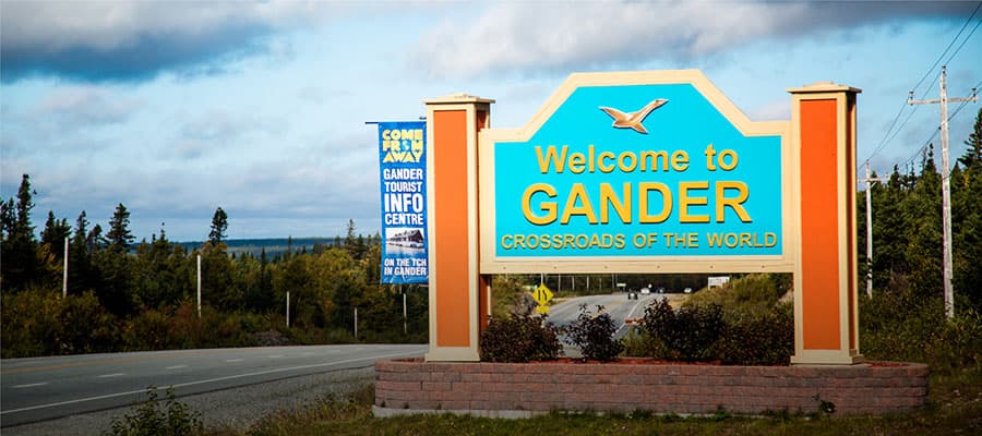 A colorful stage set shows eleven people seated in a row, surrounded by a backdrop filled with numerous square screens displaying various icons. The background is designed to resemble a forest with tree silhouettes.
