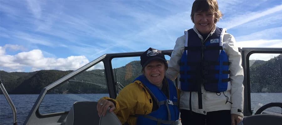 A person stands on a grassy hill overlooking the ocean, with a rugged cliffside covered in greenery to the left. The sky is dotted with clouds, and the scene conveys a sense of tranquility and vastness.
