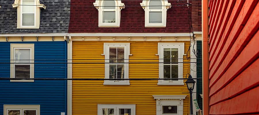 Colorful row houses with blue, yellow, and red exteriors, each featuring white window frames and trim. The street is framed on the sides by the vibrant building facades, with visible overhead utility wires crossing the scene.