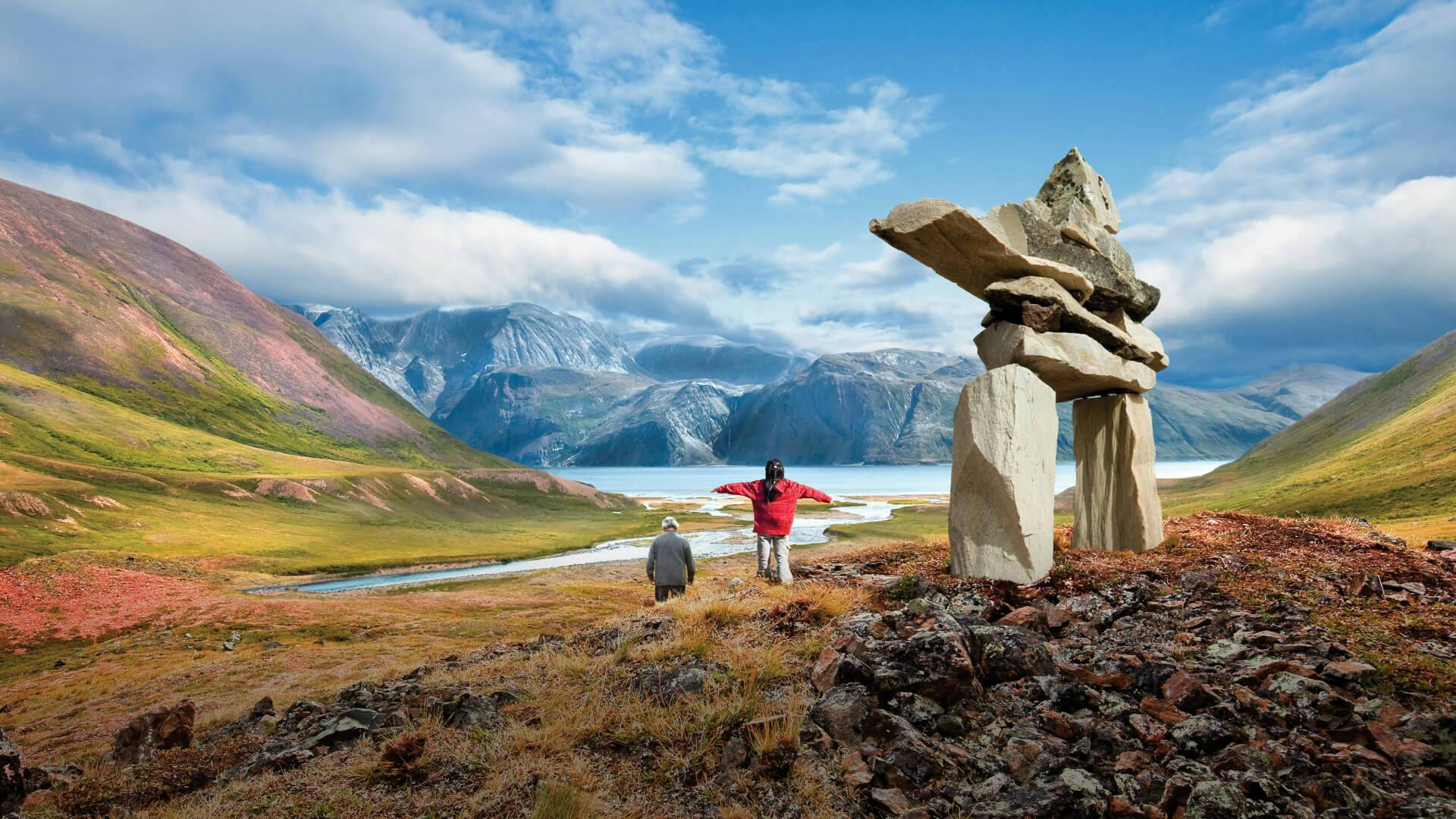 A man and child are taking in the view of the mountains beside an inukshuk in Labrador.