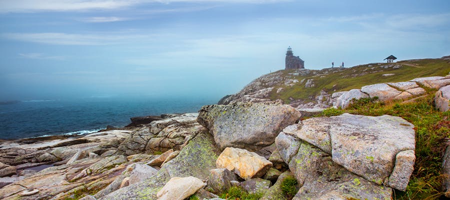 Two travellers are walking towards the granite walls of the Rose Blanche lighthouse.