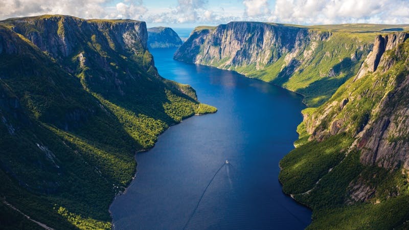 An aerial view of a boat cruising through Western Brook Pond Fjord in Gros Morne National Park.