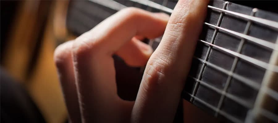 A picturesque coastal village at sunset features colorful houses near a calm body of water. Purple lupine flowers in the foreground add contrast. Mist hovers over the distant hills and small islands, creating a serene atmosphere.