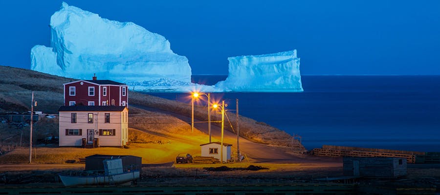 The iconic Ferryland iceberg towers behind the houses near the shoreline.