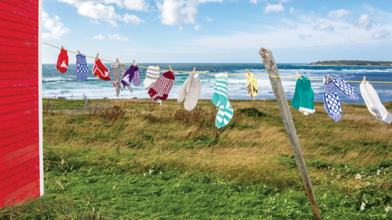 A clothesline of knitted mittens and socks swings in the wind along the coastline.