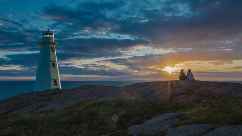 Two travellers are watching the first sunrise in North America at Cape Spear Lighthouse National Historic Site.