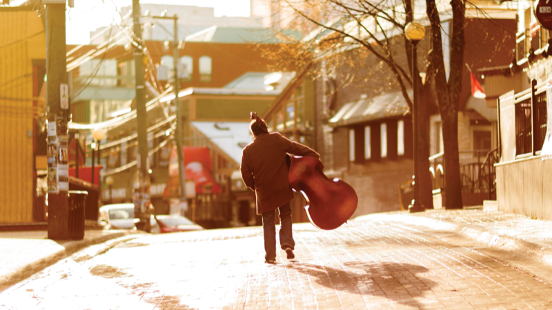 A musician is carrying a double bass down George Street in St. John’s.