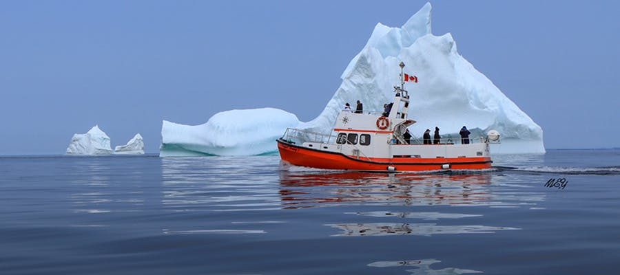 An orange and white tour boat on the water just in front of two large icebergs.