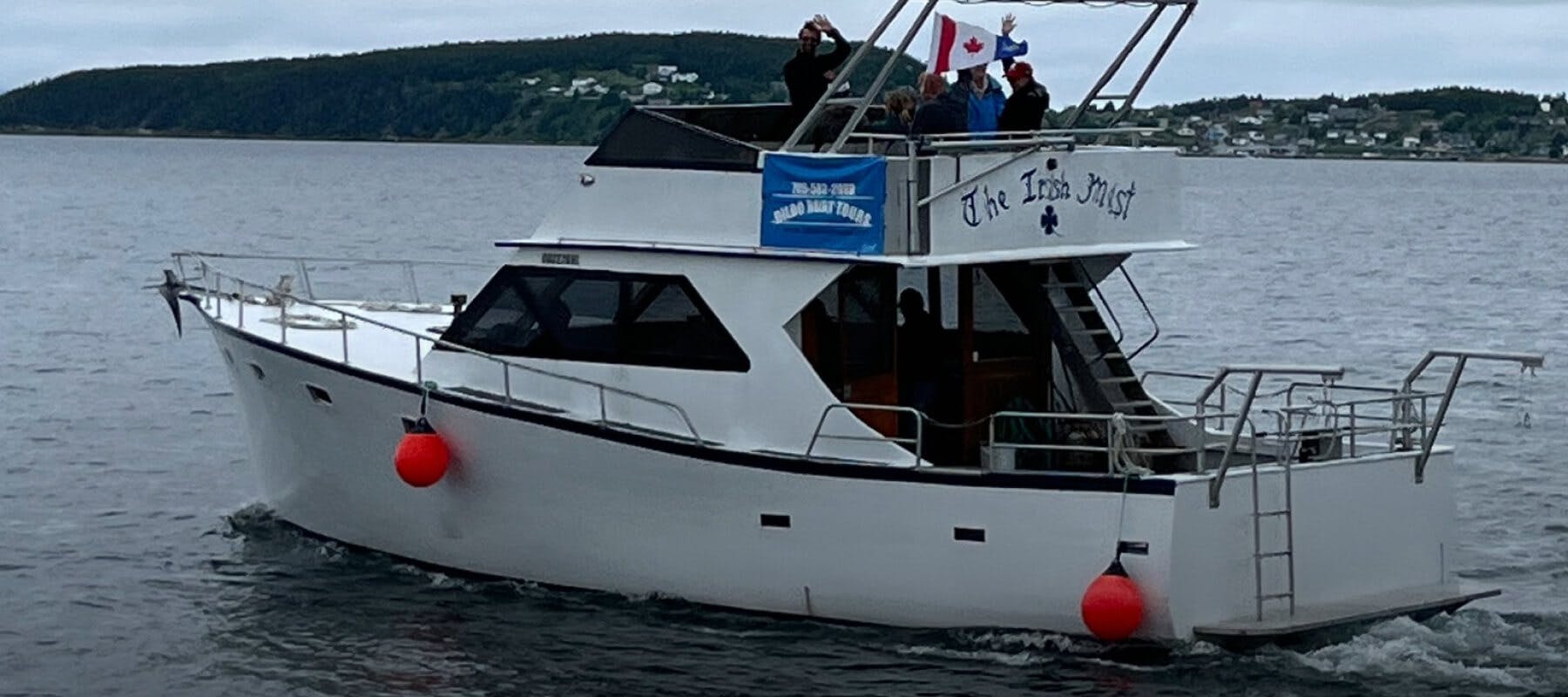 A tour boat on the water with people on the top deck celebrating and waving a Canadian flag.
