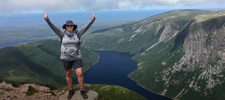 A hiker celebrating at the peak of a mountain in Gros Morne National Park.