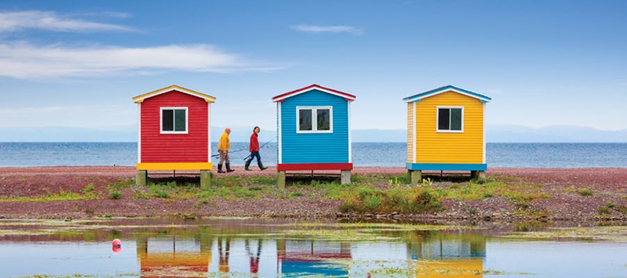 Two fishermen are walking behind colourful fishing sheds in Cavendish.